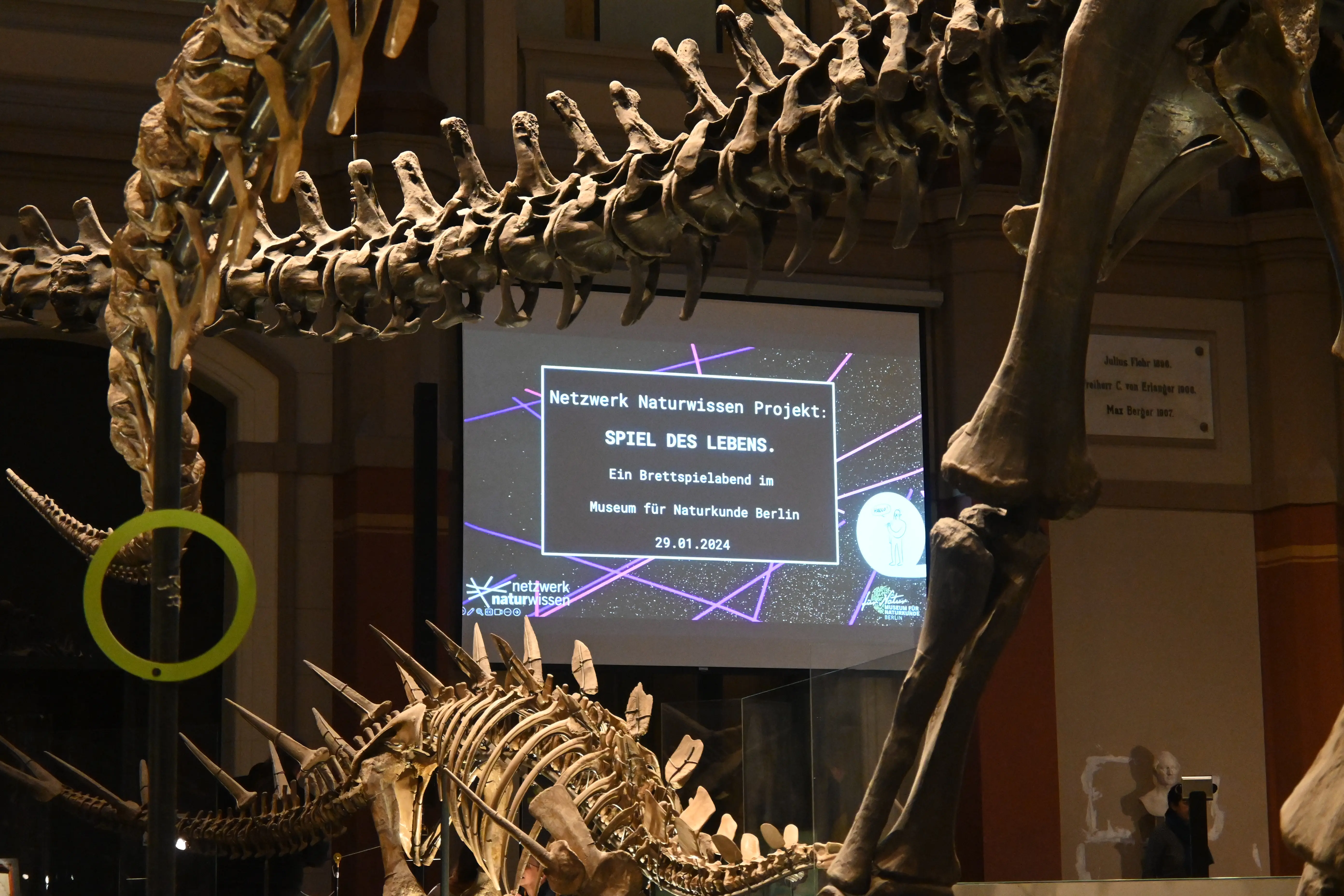 Aufnahmen des Spieleabends im Museum für Naturkunde Berlin. Die Beteiligten erklären die Thematik, Ausschnitte aus den Vorträgen sowie die Teilnehmenden beim Spielen und Interagieren werden gezeigt.