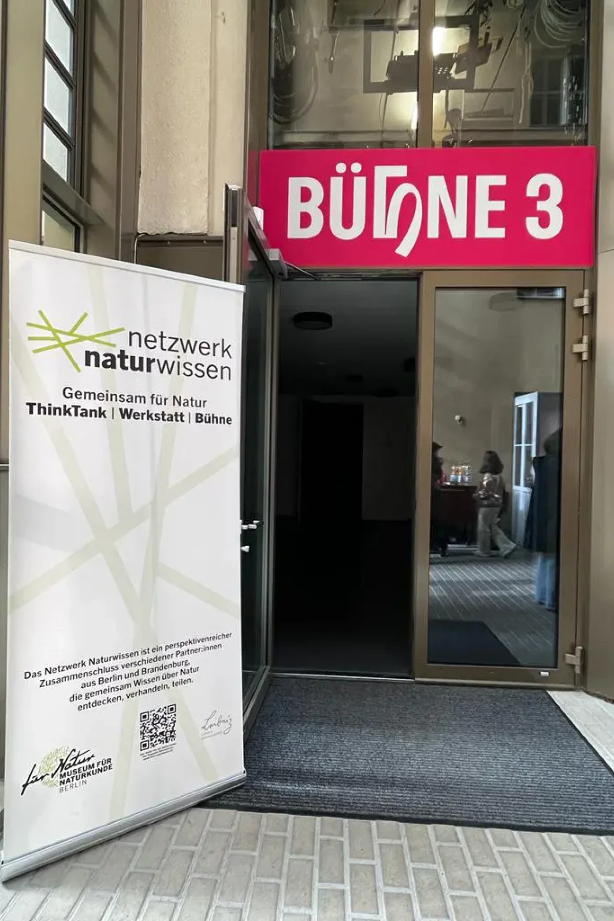 Der Eingang zum Saal “Bühne 3” des Theaters an der Parkaue wird gezeigt. Am Rand steht ein Text-Banner des Projektes Netzwerk Naturwissen.
